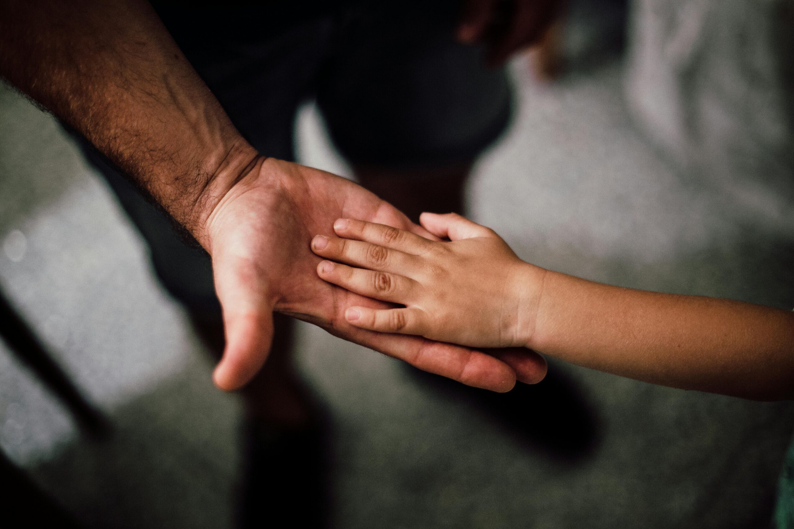 ABOUT US Close-up of a child's hand resting gently on a man's hand, symbolizing love and support.