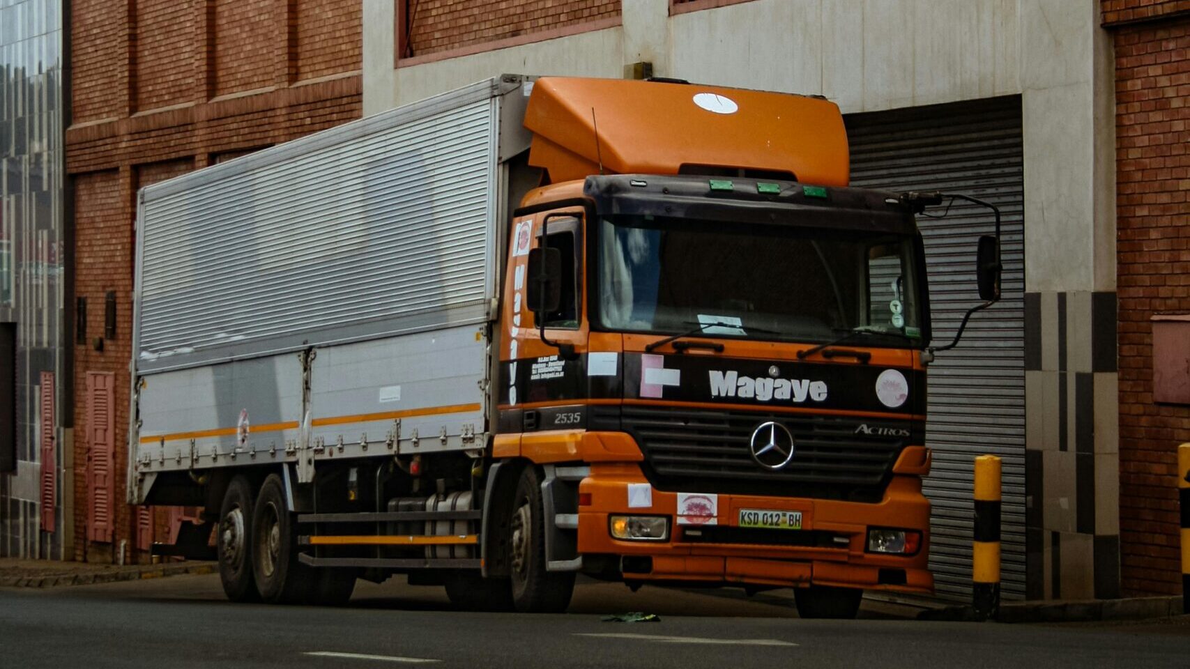 SERVICES A large orange truck parked beside a brick industrial building in Mbabane, Eswatini.